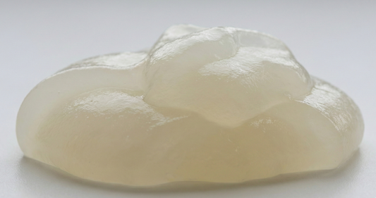 A macro, eye-level shot of a mound of translucent, off-white hydrocolloid material. The texture is thick, glossy, and slightly gelatinous, with soft ridges and a smooth, reflective surface against a clean white background.